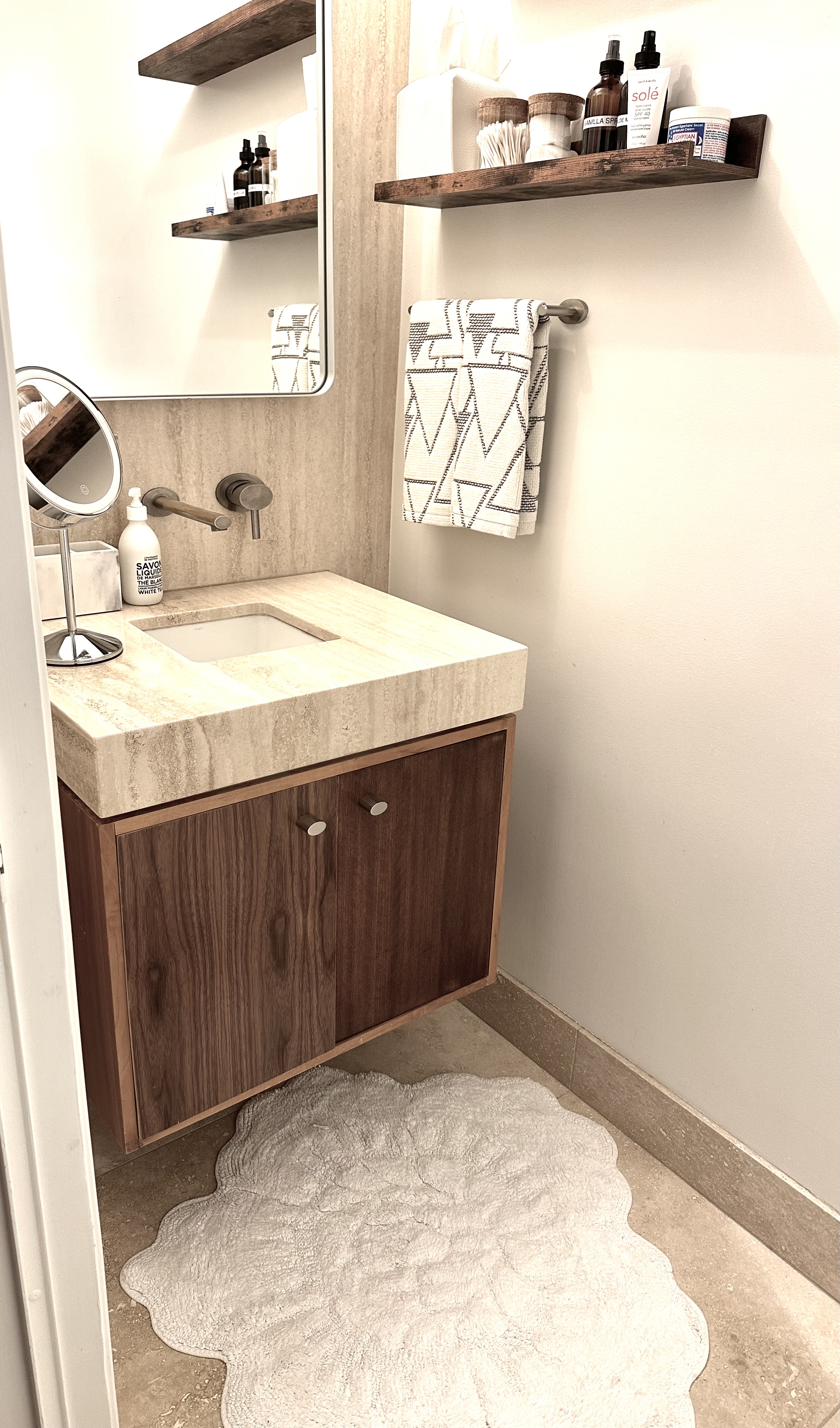Powder room vanity styled with towels and skincare on floating shelves