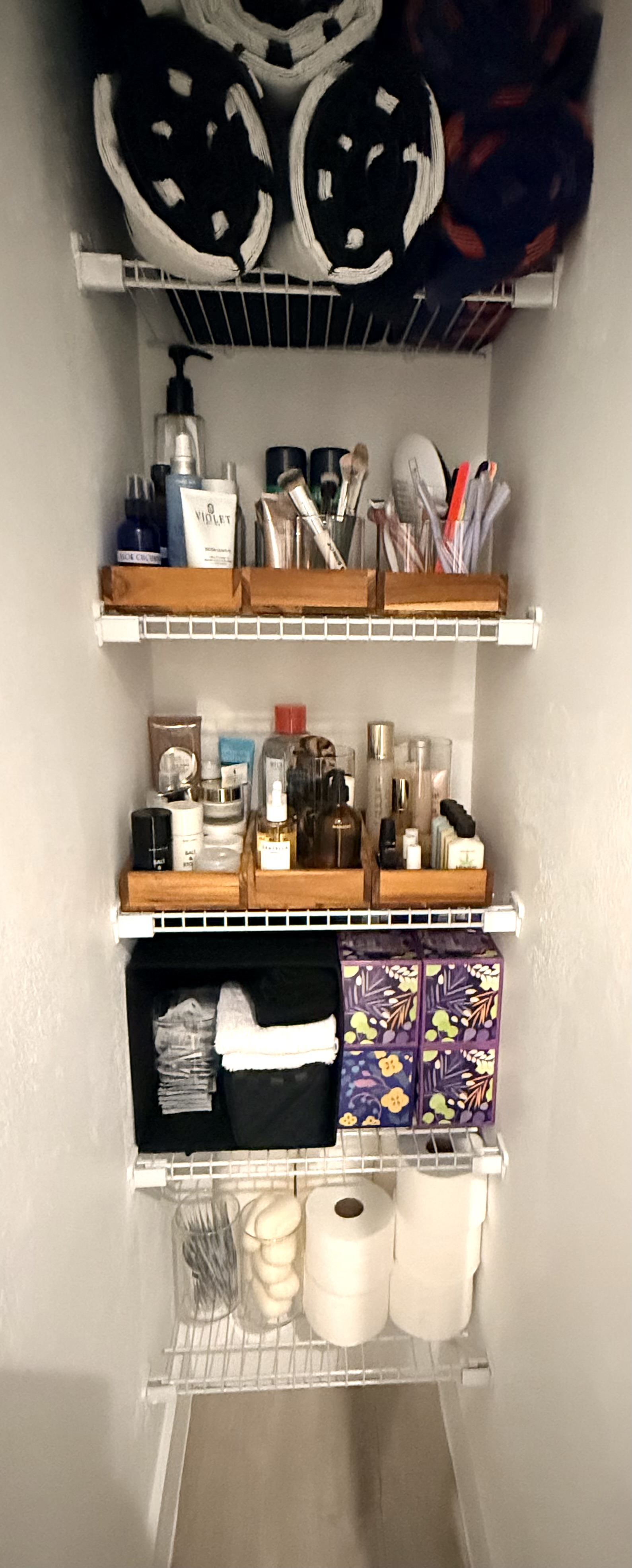 Linen closet with towels, labeled skincare trays, and organized toiletries